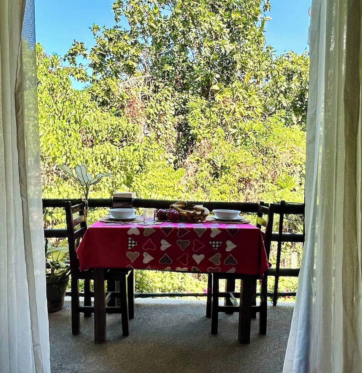 Un espace de restauration en plein air avec une table dressée pour deux personnes, entouré d’une clôture en bois et d’une végétation luxuriante.
