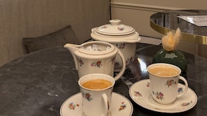 Een eetruimte met een marmeren tafel, theekopjes met bloemenmotief, een suikerpot en een koffiepot.