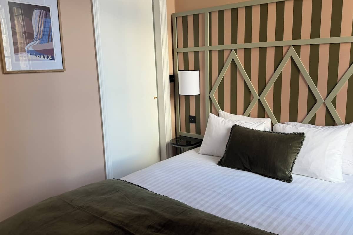 Een hotelkamer met een bed, een nachtkastje, een lamp en een ingelijst schilderij aan de muur.