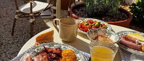 An outdoor dining area with a table set for breakfast, including plates of food, a mug, and a fruit bowl.