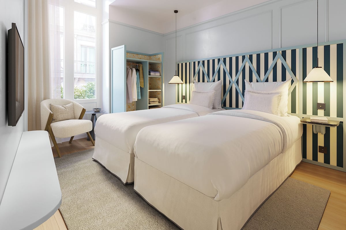 Een slaapkamer met twee bedden, een stoel, een nachtkastje, een lamp en een garderobe.