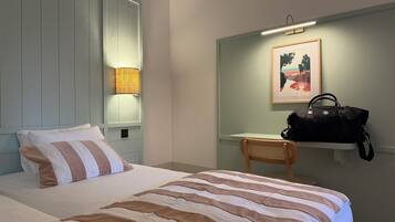 A hotel room with a bed, a desk, a chair, a lamp, and a handbag on a shelf.