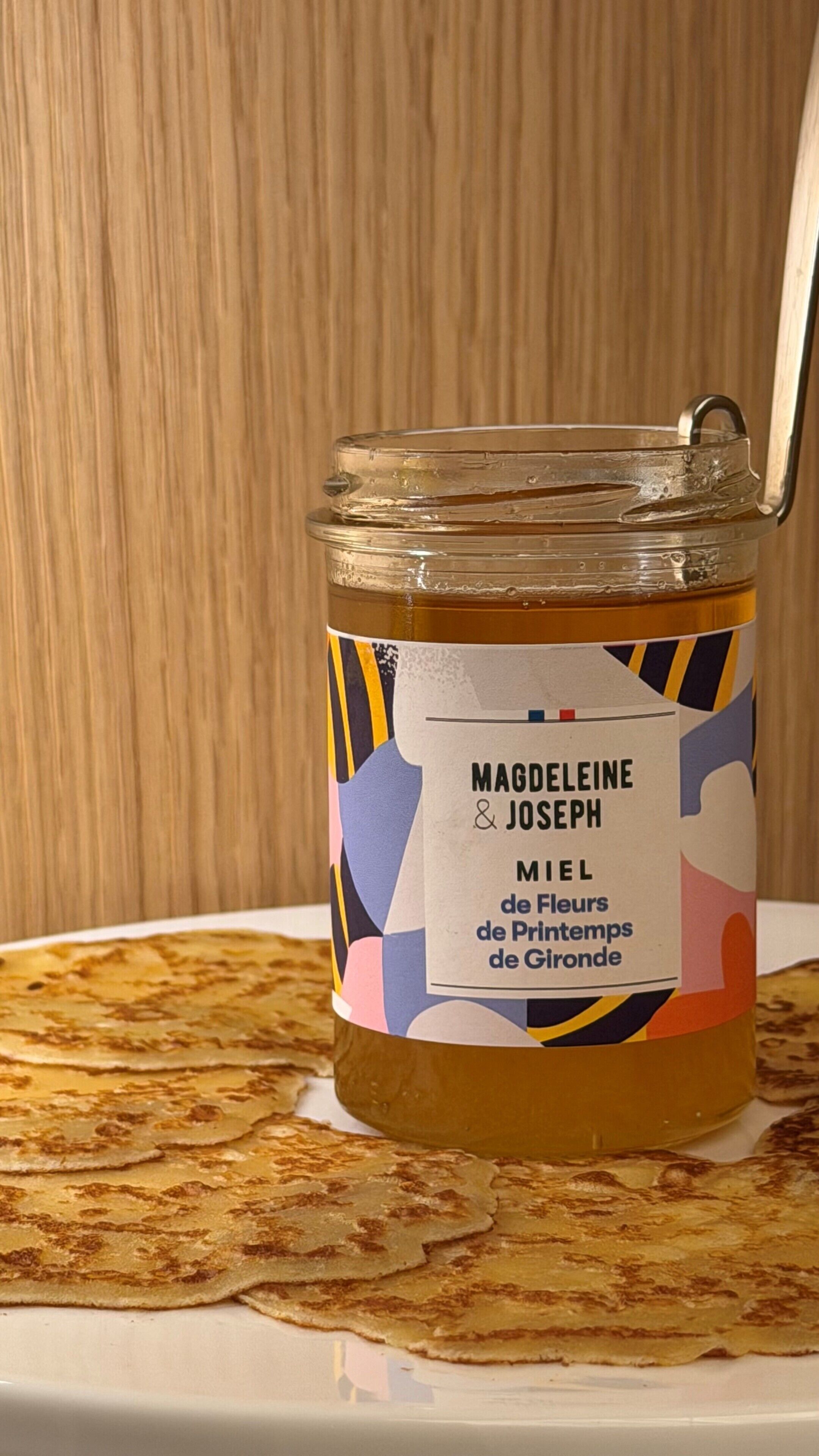 Un pot de miel avec une étiquette, posé sur une assiette avec plusieurs crêpes.