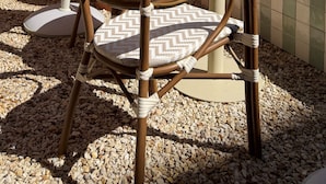Buiten zitplaatsen met rieten stoelen en een grote roze parasol, omringd door groen en een betegeld terras.