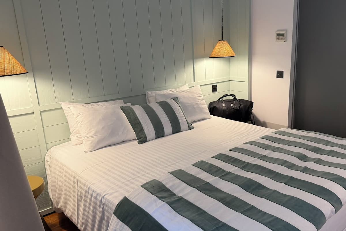 Een netjes opgemaakt bed met een gestreept sprei, een hoofdbord met verticale lijnen en twee aan de muur bevestigde lampen.
