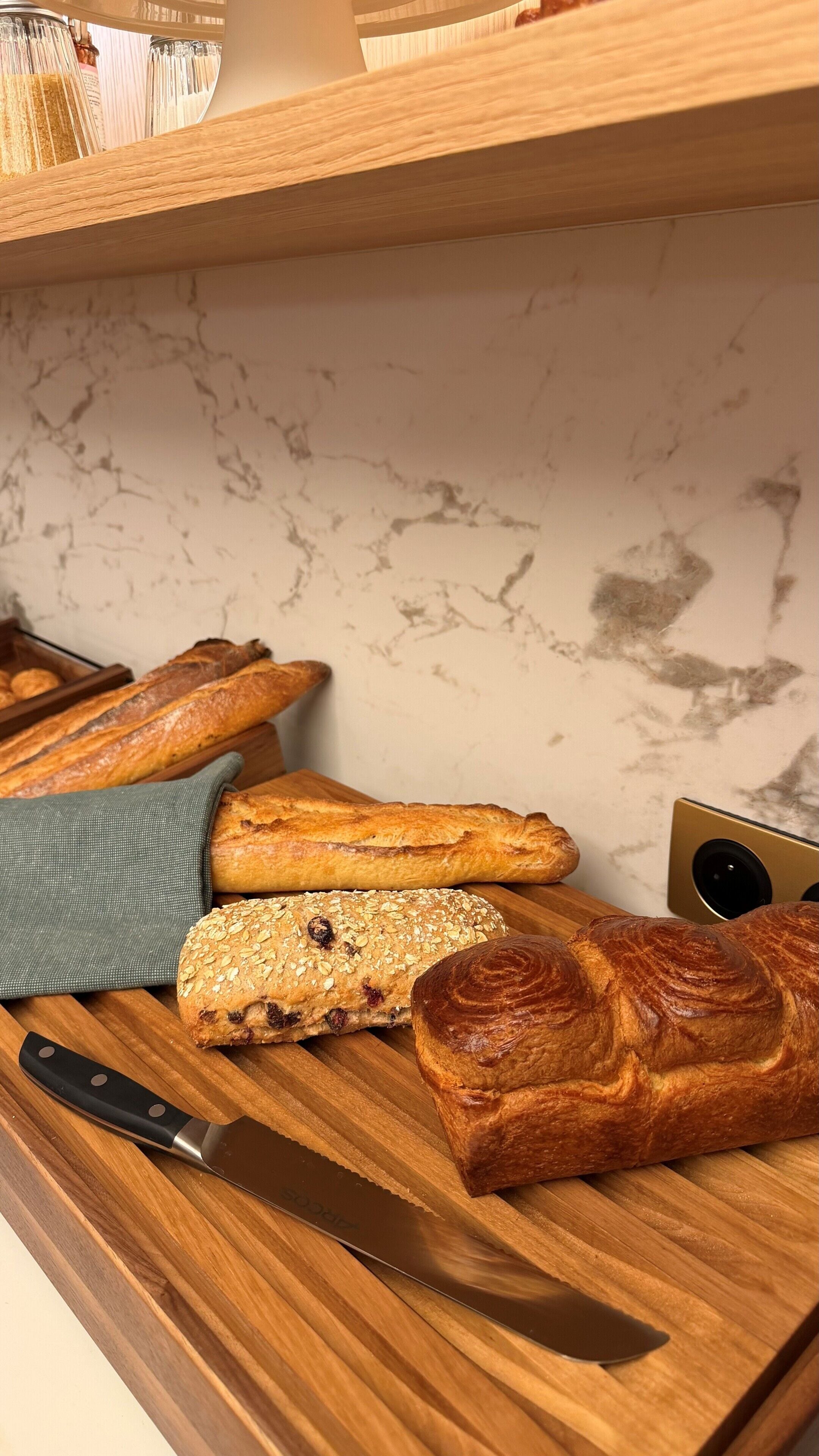 A wooden cutting board with various baked goods, a knife, and a marble wall in the background.