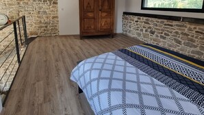 Een slaapkamer met een houten kledingkast, een bed met beddengoed met een patroon, een hanglamp en een stenen muur.