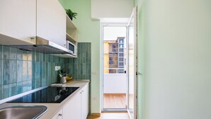 A narrow kitchen with a black countertop, white cabinets, and a view to a balcony. - Il Ciucciariello (Naples)