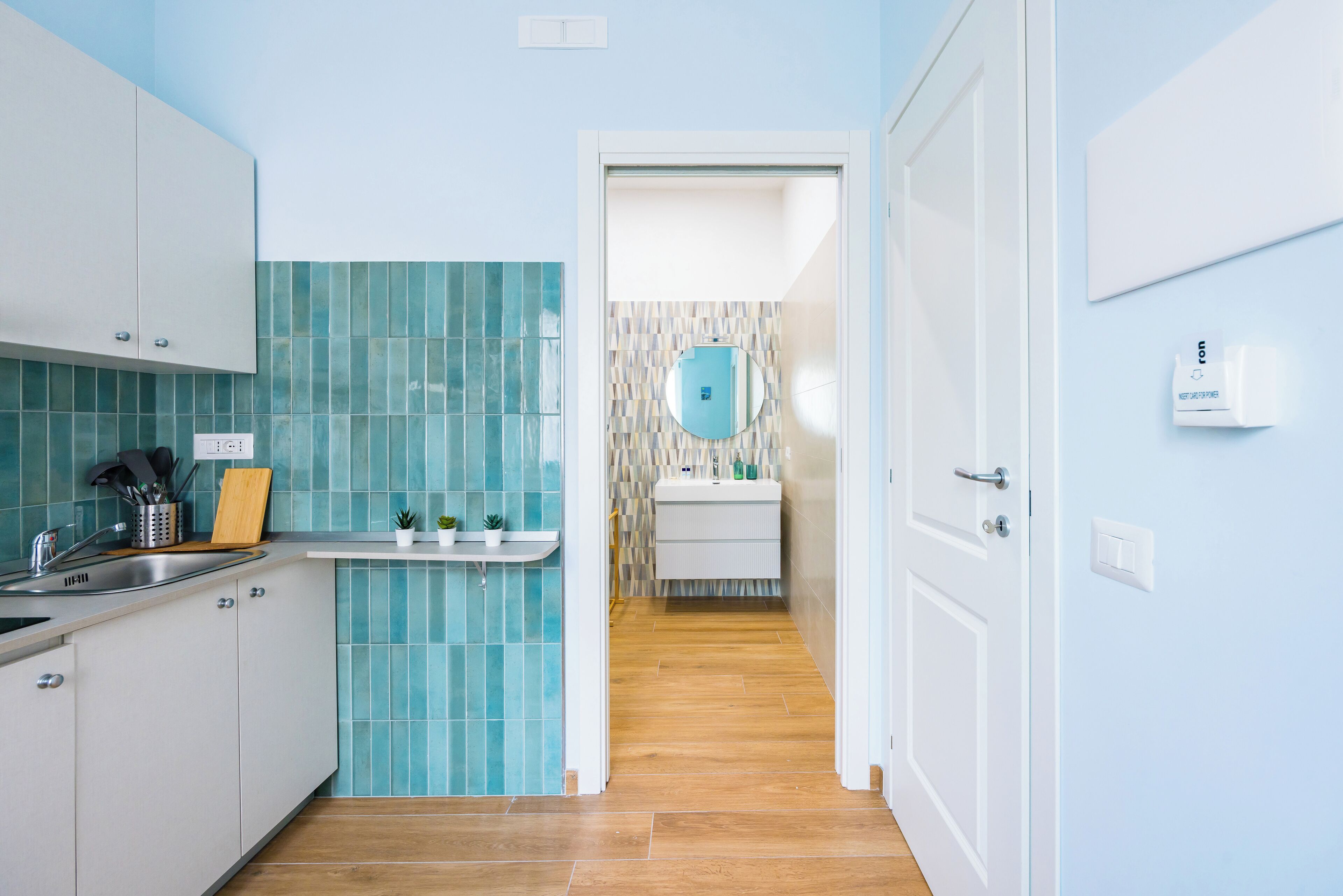 A modern kitchen with white cabinets, a blue tiled backsplash, and a wooden floor.