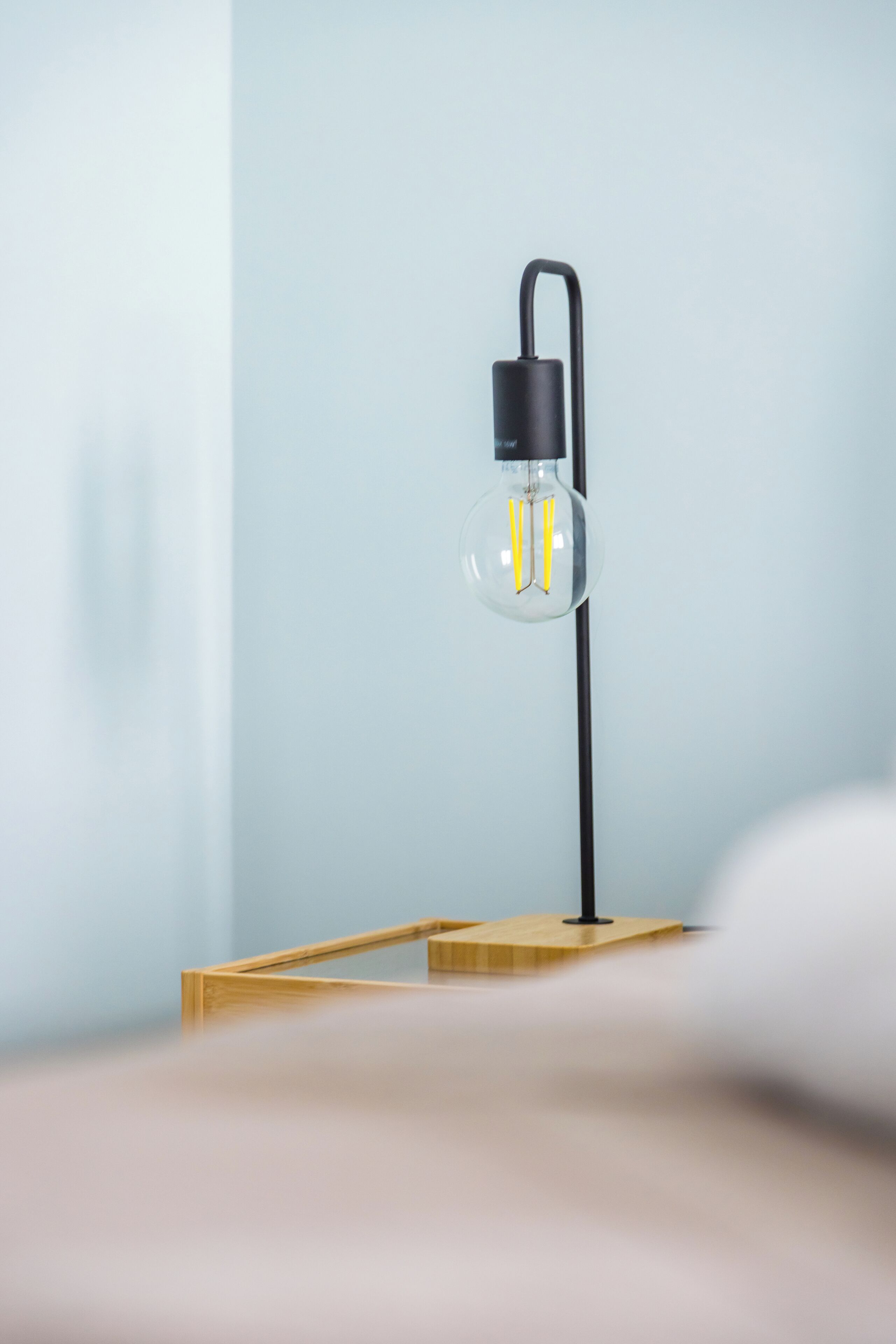 A modern lamp with a clear glass shade and a black base, placed on a wooden platform.