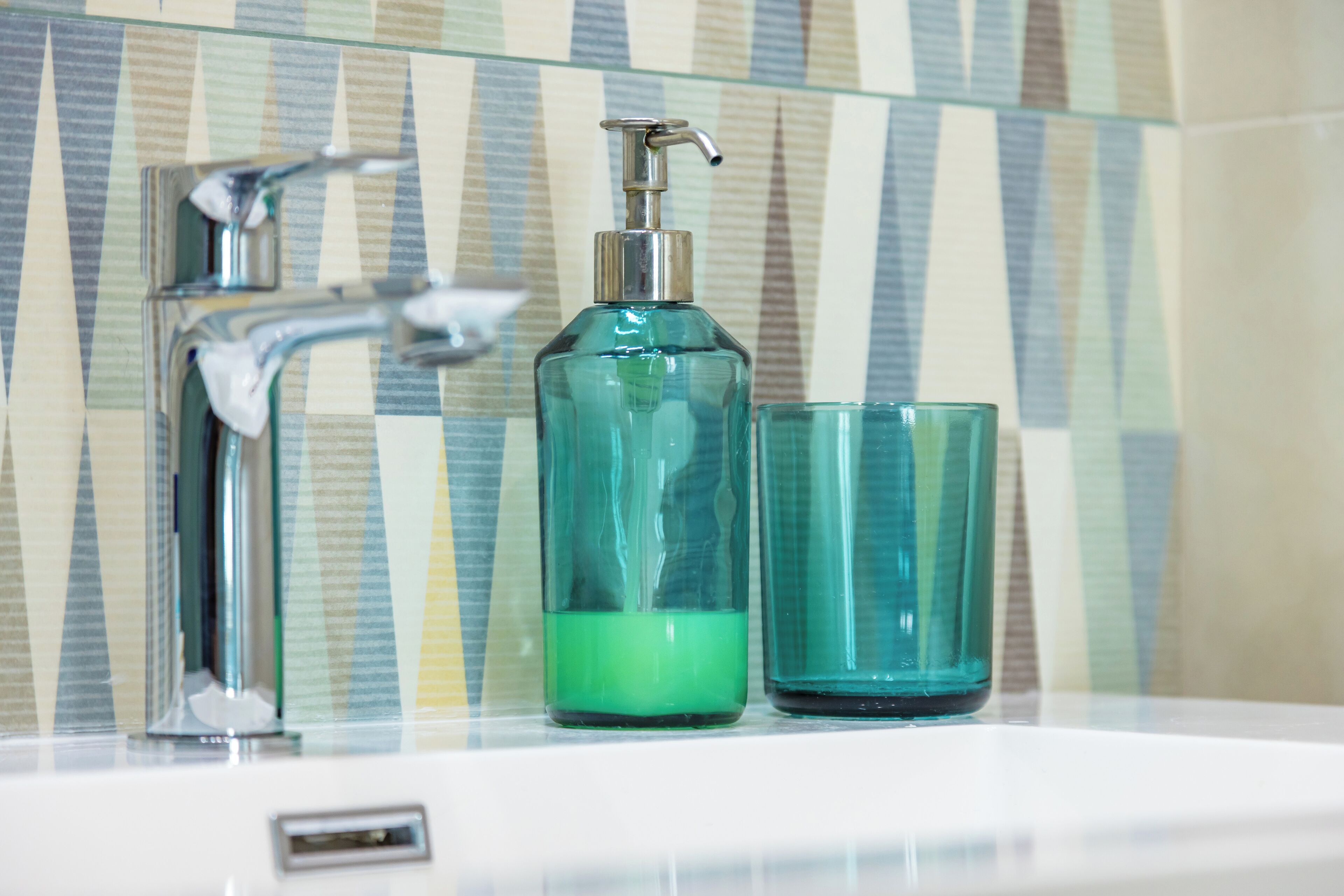 Ein Badezimmer mit einem modernen Wasserhahn, einer transparenten Seifenspenderflasche und einem passenden Glas.