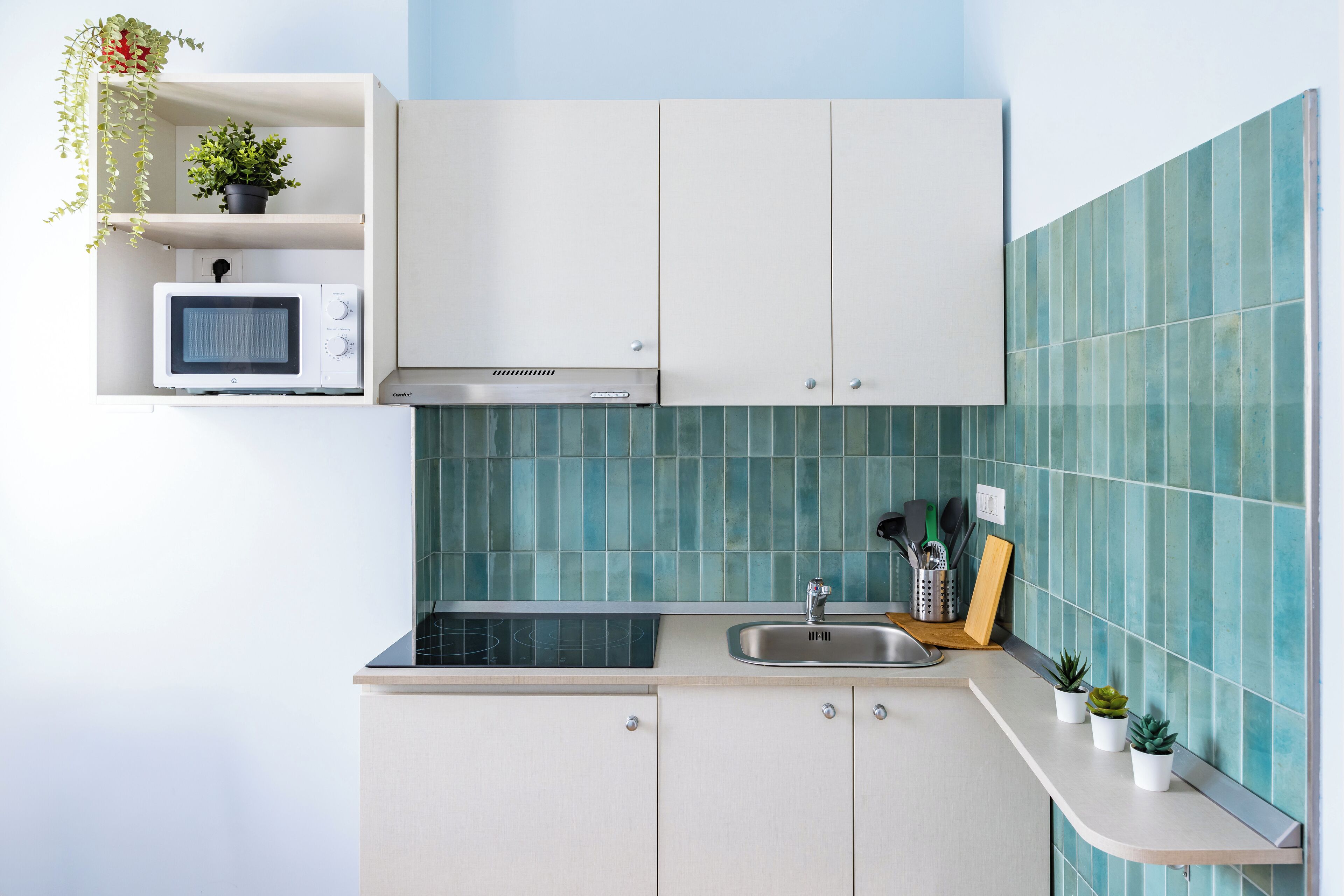 A kitchen with white cabinets, a microwave, a sink, and a backsplash with blue tiles.