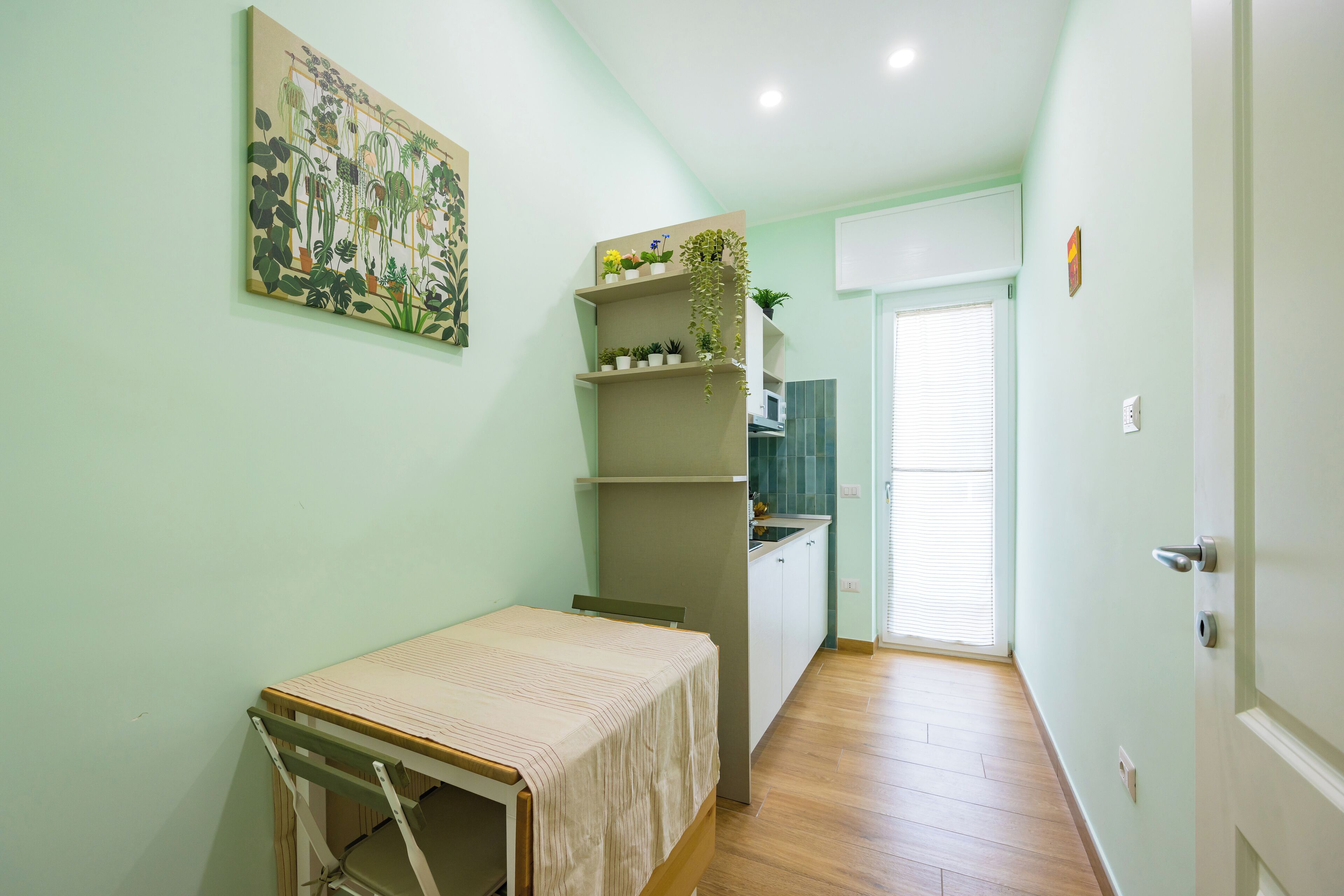 A narrow hallway with a bed, a shelf with plants, and a door leading to a bathroom.