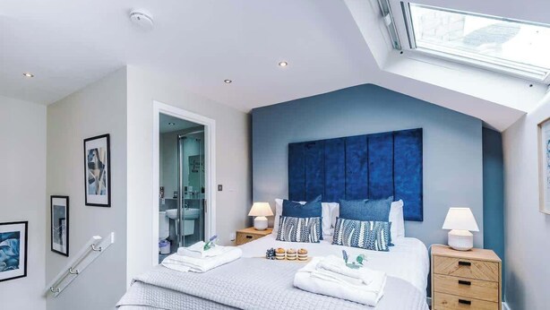 Een moderne slaapkamer met een groot bed, nachtkastjes, een dakraam en een zichtbare badkamer door een open deur.