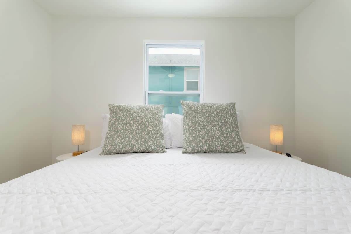 A neatly made bed with a white quilted cover, two patterned pillows, and two bedside lamps on white nightstands.