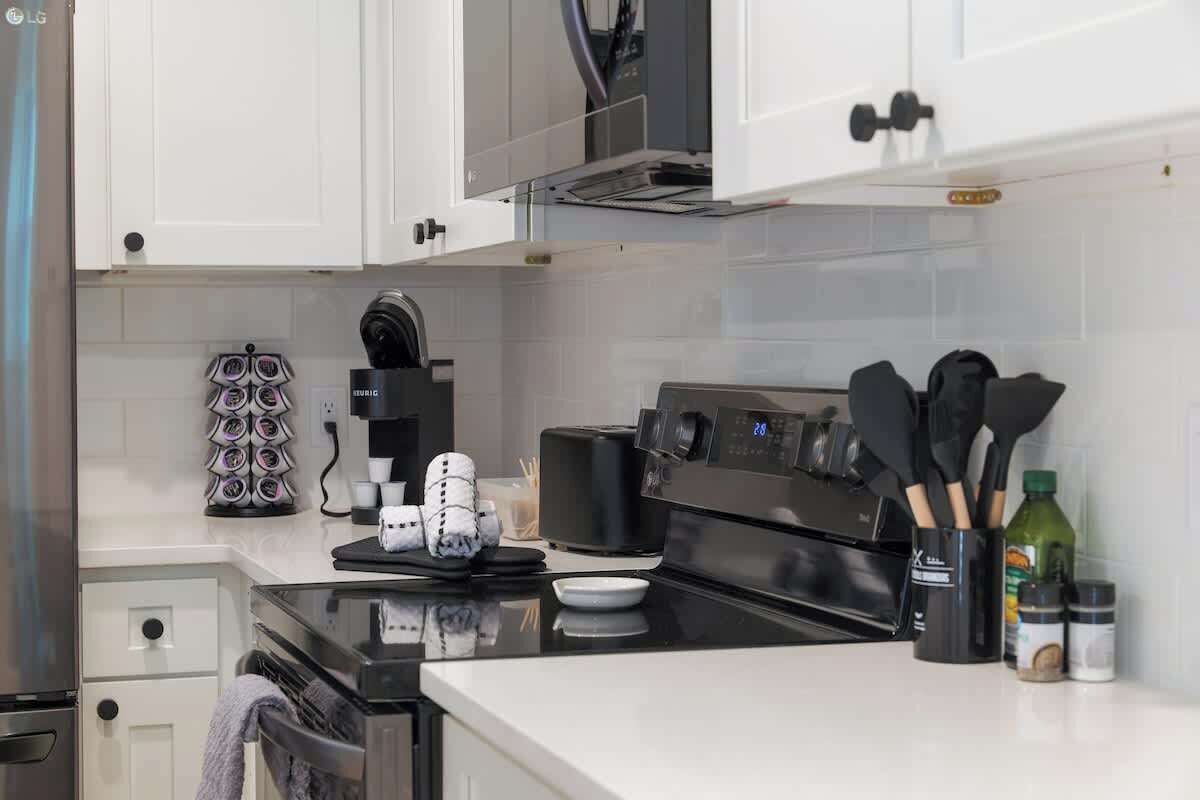 A modern kitchen with white cabinets, a black stove, and various kitchen utensils.