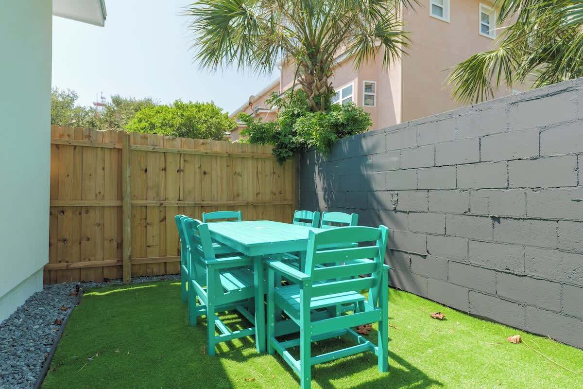 Une terrasse avec une clôture en bois, une table et des chaises vertes, et un mur gris.