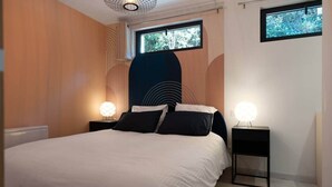 Un dormitorio moderno con una cama grande, dos mesitas de noche con lámparas, una ventana con vistas a árboles y un diseño de pared único.