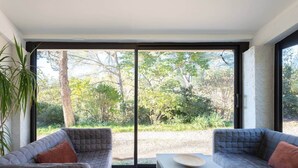 Una habitación moderna con dos sofás grises, una mesita blanca y un amplio ventanal corredero que da a un jardín.