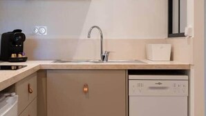 Una cocina compacta con lavavajillas, cafetera y un armario con espejo sobre el lavabo.
