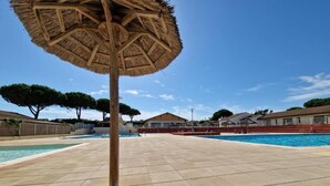A pool area with a thatched umbrella, tiled flooring, and surrounding trees.
