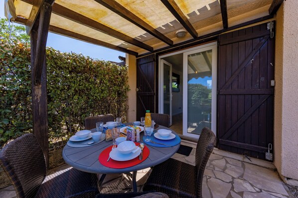 An outdoor patio with a round table set for dining, surrounded by wicker chairs.