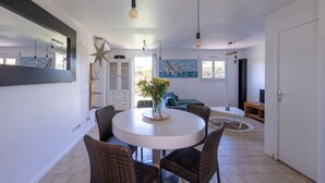 A dining area with a round table, wicker chairs, a vase with flowers, and a painting on the wall.