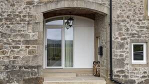 Ein Steinhaus mit einem großen Bogenportal, einer weißen Tür mit Glasfeldern und einem kleinen Fenster rechts.