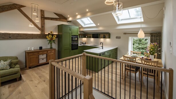 Eine moderne Küche mit grünen Schränken, einem Essbereich aus Holz und einer Treppe, die zu einer oberen Ebene führt.