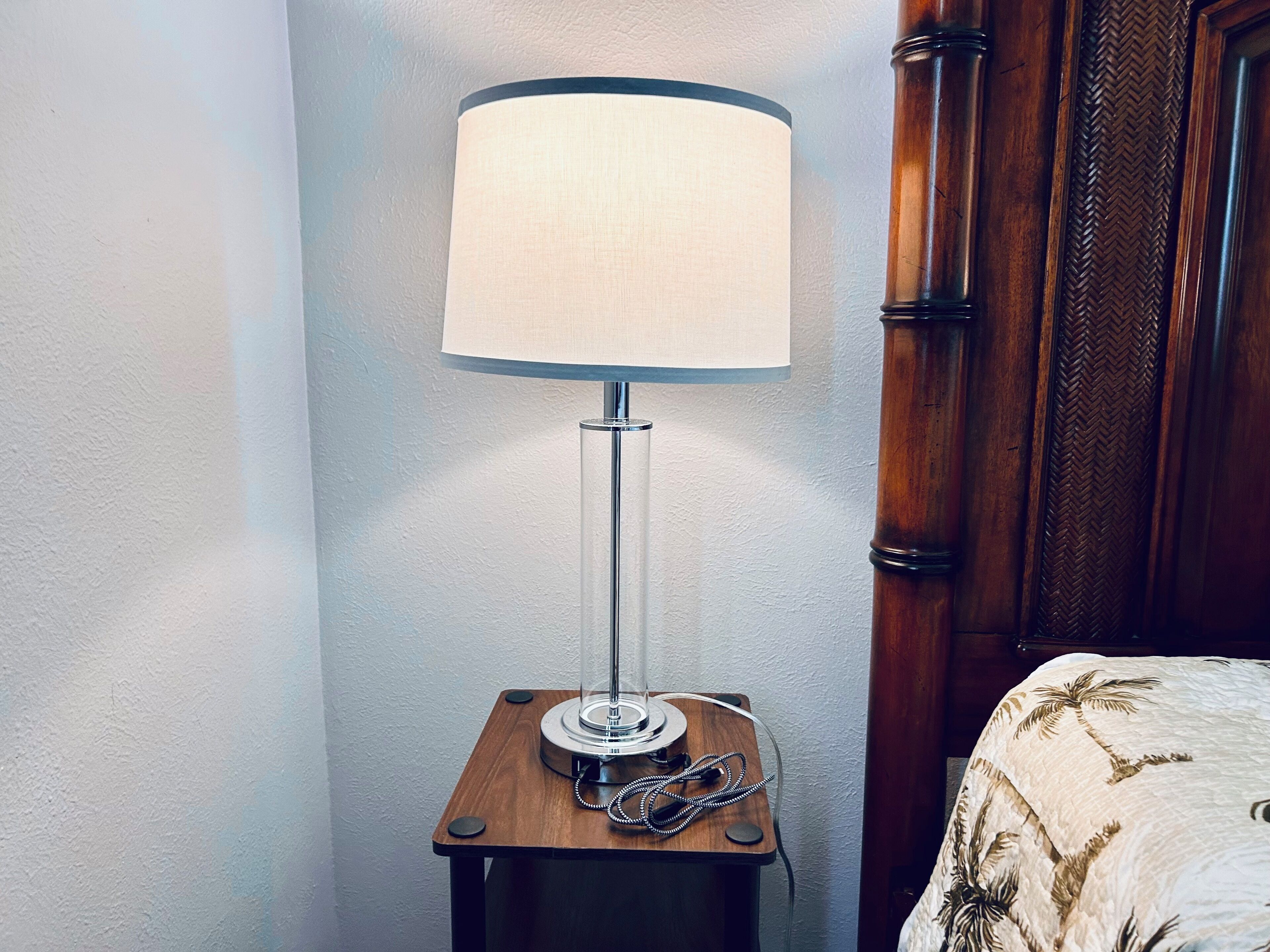 A corner of a room with a wooden nightstand holding a lamp and a telephone.