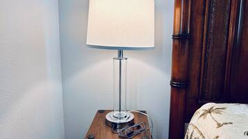 A corner of a room with a wooden nightstand holding a lamp and a telephone.