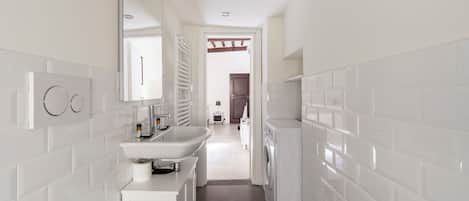 A modern bathroom with white tiles, a sink, a mirror, and a washing machine.