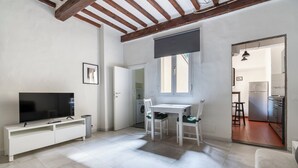 A modern living room with a flat-screen TV, white furniture, a dining area, and a kitchen visible through an open doorway. - Pinzochere 16 N - Studio Apartment, Sleeps 2 (Firenze)