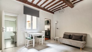 A modern living room with a white dining table, two chairs, a grey sofa, and a kitchen in the background. - Pinzochere 16 N - Studio Apartment, Sleeps 2 (Firenze)