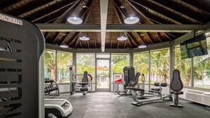 Un gimnasio con diverso equipo de ejercicio, ventanas amplias y vistas a zonas verdes.
