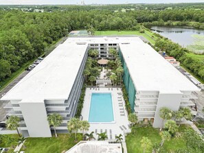 A modern hotel with a central pool, surrounded by lush greenery and a lake view.