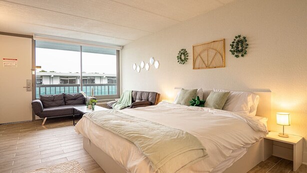 A modern bedroom with a large bed, a sofa, a nightstand, and a view of the outside.