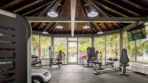 A gym with various exercise equipment, large windows, and a view of greenery outside.