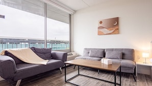 Un soggiorno moderno con un divano grigio, un tavolino in legno e vista mare attraverso ampie finestre.