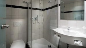 A modern bathroom with a glass-enclosed shower, a white toilet, and a sink with a mirror above it. - Boardinghouse calf stretcher (Altdorf)