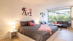 Ein modernes Schlafzimmer mit einem großen Bett, Nachttischen, einer Couch und Blick auf Grün.