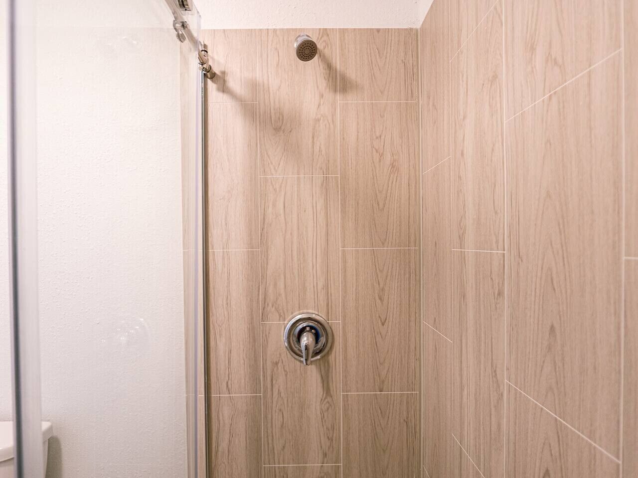 A shower with a wooden panel wall and a visible showerhead.