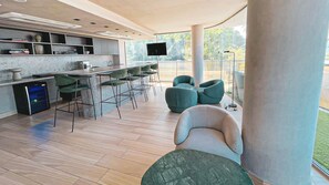 A modern kitchen with a bar area, green chairs, and a large window overlooking a garden. - Setai Yacht S3 - By Almare Flats (João Pessoa)