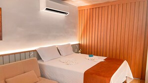 Et hotelværelse med seng, et natbord, en aircondition samt en væg med træpaneler.