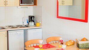 A compact kitchen with a microwave, toaster, and coffee maker. There is a dining table with chairs, a small table with a candle, and a magazine. - travelski home classic - Résidence Les Balcons d'Anaïs 3* - 3 pièces 4/6 personnes (Villarodin-Bourget)