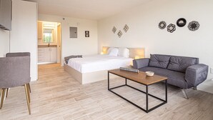 A modern, well-lit room with a bed, a gray sofa, a wooden coffee table, and a small dining table with chairs. - Kissimmee Affordable Disney Retreat with Lake View (Kissimmee)