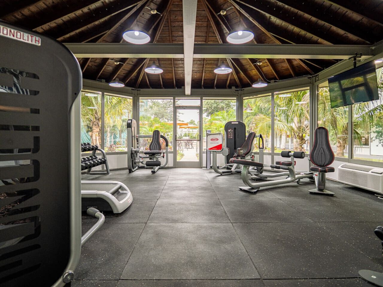 A gym with various exercise equipment, large windows, and a view of greenery outside.