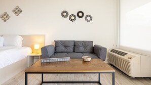 A modern hotel room with a bed, a bedside table with a lamp, a grey sofa, a wooden coffee table, and decorative wall art. - Kissimmee Affordable Disney Retreat with Lake View (Kissimmee)