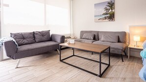 A modern living room with a grey sofa, a wooden coffee table, and a painting of a beach scene.