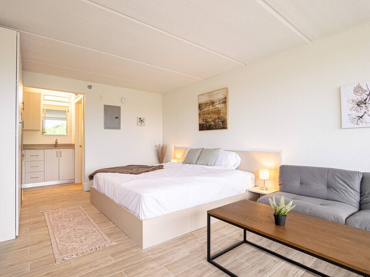 A bedroom with a bed, bedside table, lamp, and a grey sofa.